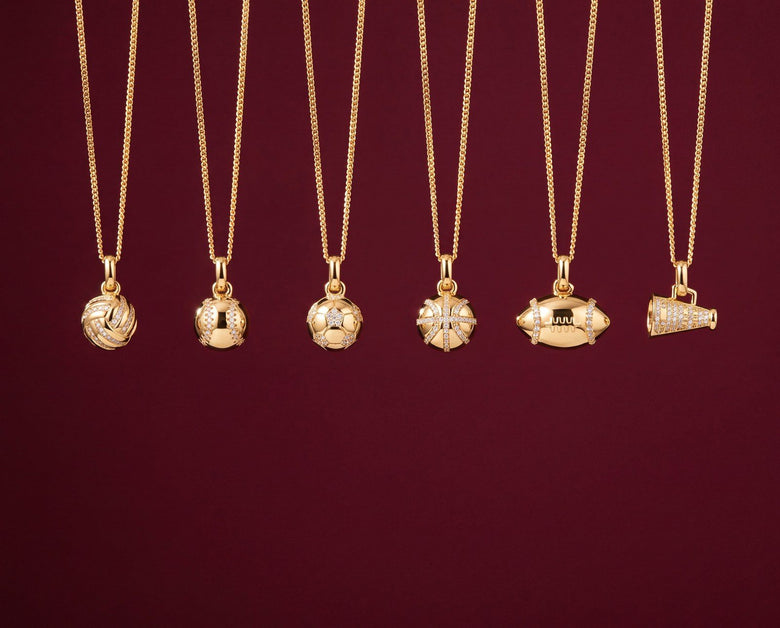 Six gold sport pendant necklaces (volleyball, baseball, soccer ball, basketball, football and megaphone) on burgundy