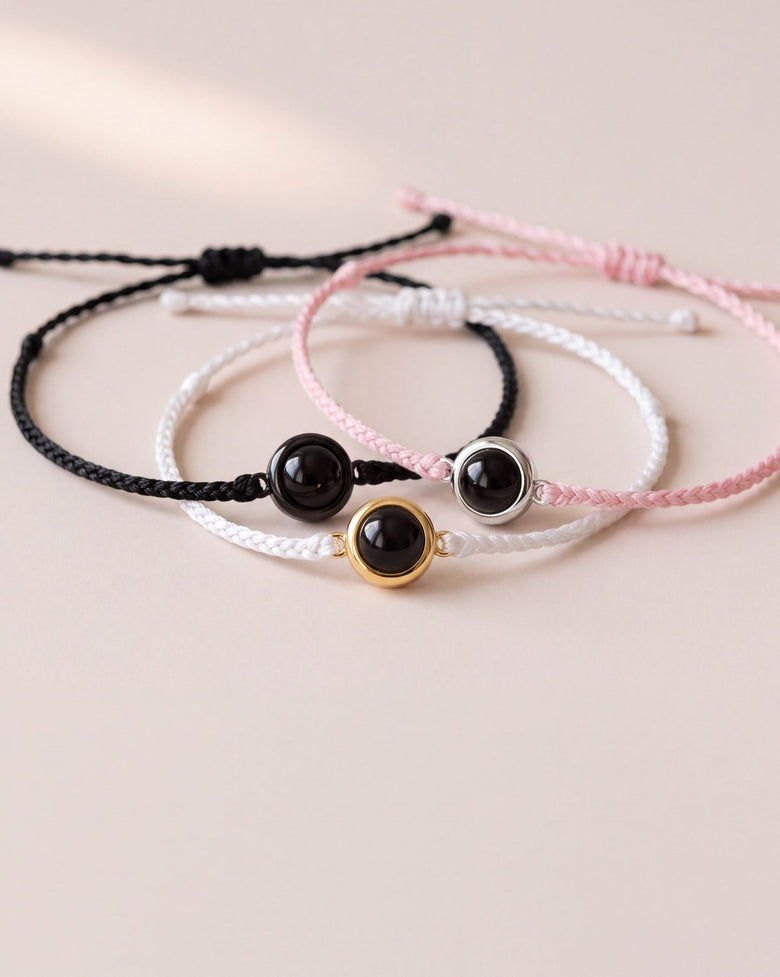 Black, white and pink braided photo bracelets, each with a black photo gem, on a blush background